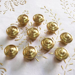 May include: Ten gold-toned metal cabinet knobs with a rounded, domed top. The knobs are arranged in a circular pattern on a white surface.