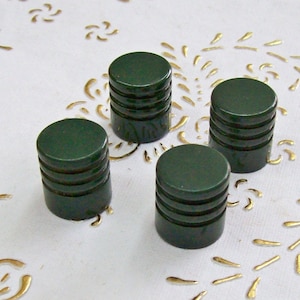 Puede incluir: Cuatro pomos redondos de color verde oscuro con un diseño acanalado. Los pomos están dispuestos en forma de cuadrado sobre una superficie blanca con un patrón dorado.