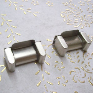 Op de afbeelding: Twee zilveren metalen horlogeband schakels. De schakels zijn rechthoekig met afgeronde randen en een klein gaatje aan elke kant.