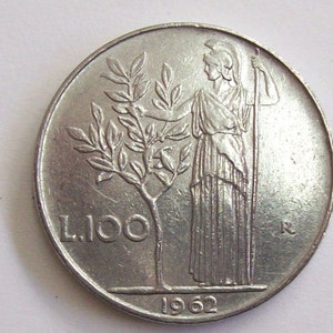 Puede incluir: Una moneda italiana de plata con la inscripción "L. 100" y el año "1962". La moneda muestra a una mujer sosteniendo un bastón y un árbol con hojas.