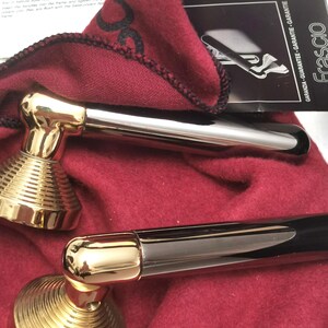 May include: Two door handles with a gold-colored base and a silver-colored handle. The handles are resting on a red cloth. A black and white tag with the word "FRASCIO" is visible.