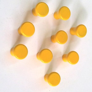 May include: Nine yellow ceramic knobs with a rounded top and a short stem. The knobs are arranged in a loose circle on a white background.