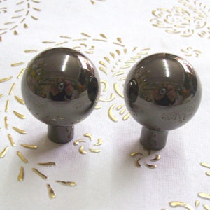 May include: Two black round cabinet knobs with a shiny finish. The knobs have a small stem extending from the bottom.