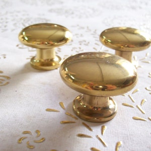 May include: Three gold-toned cabinet knobs with a rounded oval shape and a short, cylindrical base.