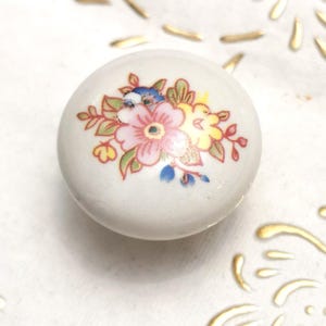 May include: White ceramic knob with a floral design featuring pink, yellow, and blue flowers. The knob is round and has a smooth surface.