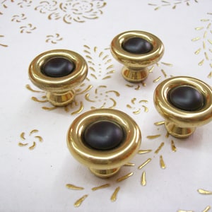 Peut inclure: Quatre boutons de cabinet dorés avec un centre brun foncé. Les boutons ont une bordure surélevée autour du centre.