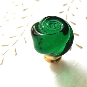 Puede incluir: Un pomo de armario de vidrio verde en forma de rosa con una base dorada.