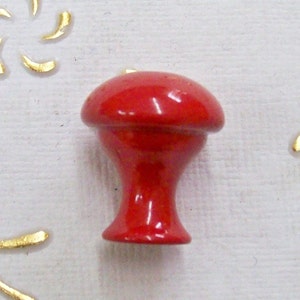 Pode incluir: Um botão de cerâmica vermelho em forma de cogumelo. O botão tem um acabamento liso e brilhante.