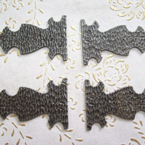 Puede incluir: Cuatro soportes de esquina de metal de estilo antiguo con un acabado texturizado martillado. Los soportes son de color gris oscuro y tienen un diseño decorativo y ornamentado.