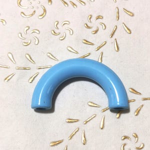May include: A light blue plastic handle with a rounded shape. The handle has two holes on either end.