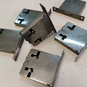 Peut inclure: Six plaques de serrure de porte en métal argenté avec des trous de serrure. Les plaques sont rectangulaires et ont une surface légèrement texturée.