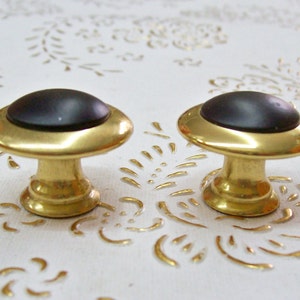 Peut inclure: Deux boutons de porte en or avec des dessus ronds noirs. Les boutons ont un design simple et classique.