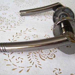 May include: A black door handle with a polished finish. The handle has a curved design and a round knob.