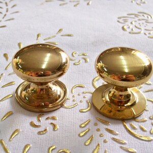 May include: Two gold-toned cabinet knobs with a round, slightly domed top and a circular base.