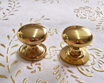 May include: Two gold-toned cabinet knobs with a round, slightly domed top and a circular base.