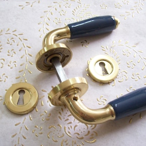 May include: Two brass door handles with blue ceramic knobs. The handles are in the shape of a lever and have a keyhole on the front. The handles are on a white surface.