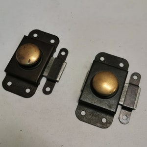 Op de afbeelding: Twee zwarte metalen deursloten met goudkleurige knoppen. Elk slot heeft een apart metalen stuk dat in het slot schuift om het te vergrendelen.