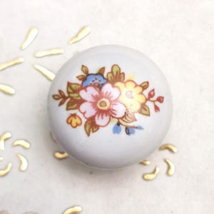 May include: White ceramic knob with a floral design. The flowers are pink, yellow, and blue with green leaves.