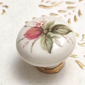 Può includere: Pomo in ceramica bianca con un design floreale con fiori rosa e verdi. Il pomo ha una base dorata.