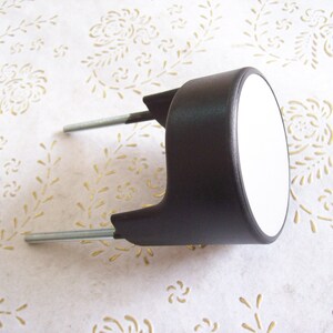 May include: Black plastic bike seat post with two silver metal bolts. The seat post has a white circular reflector.