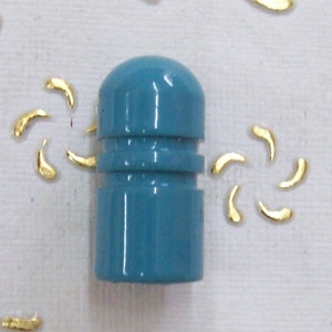 Puede incluir: Un tapón de botella de plástico azul verdoso con la parte superior redondeada y un anillo elevado en el medio.