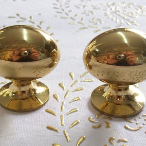 May include: Two gold oval-shaped cabinet knobs with a round base. The knobs are polished and reflect the surrounding environment.