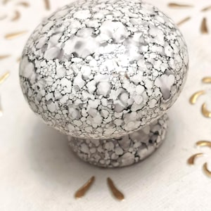 May include: White ceramic knob with a speckled pattern. The knob is round with a slightly raised base.