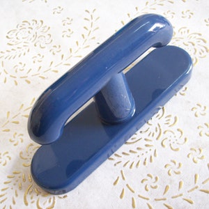 Puede incluir: Una manija de puerta de plástico azul con una base redondeada de forma ovalada y una manija rectangular elevada.