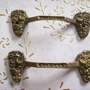 May include: Two antique brass cabinet pulls with grapevine and leaf designs. The pulls have a decorative, ornate design.