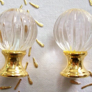 Puede incluir: Dos pomos de armario de cristal transparente con bases doradas. Los pomos tienen un diseño acanalado y son redondos.