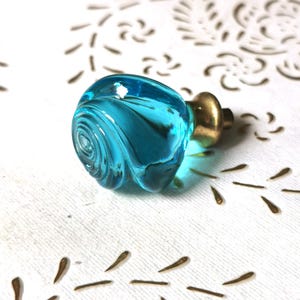 Könnte beinhalten: Ein türknopf aus türkisblauem Glas mit einem goldenen Metallsockel. Der Knopf hat ein Spiralmuster.