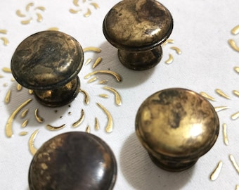 May include: Four antique brass cabinet knobs with a worn, distressed finish. The knobs have a round top and a short, cylindrical base.