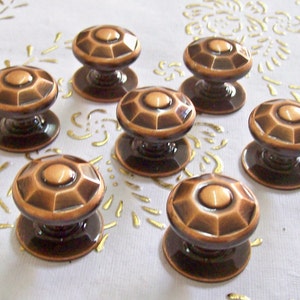 May include: Seven antique copper cabinet knobs with a faceted design. The knobs have a dark brown patina and are arranged on a white surface.