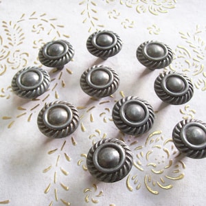 Può includere: Dieci pomelli per mobili in argento con un design circolare in rilievo. Ogni pomello ha un bordo a corda.