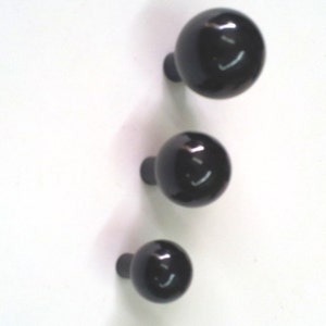 Op de afbeelding: Drie zwarte ronde knoppen met een glanzende afwerking. De knoppen zijn bevestigd aan een wit oppervlak.