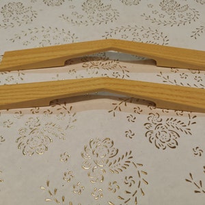 Peut inclure: Deux poignées de porte de placard en bois avec une finition brun clair. Les poignées sont en forme d'arche avec une découpe au centre.