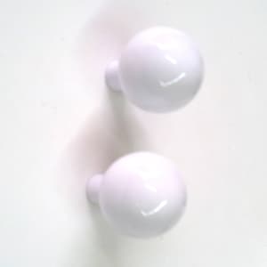 Peut inclure: Deux boutons en céramique blanche de forme ronde et lisse. Les boutons sont conçus pour être utilisés sur des meubles ou des armoires.
