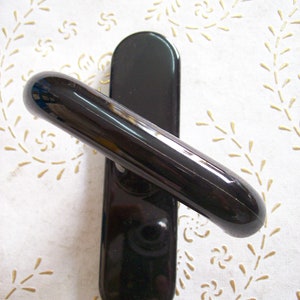 Puede incluir: Pomo de puerta negro con una palanca curva. El pomo está hecho de un material liso y brillante.