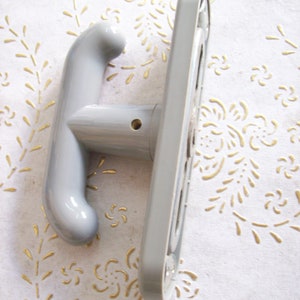 Puede incluir: Una manija de puerta de plástico gris con un diseño curvo. La manija tiene un pequeño agujero en el centro para un tornillo.