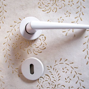 Può includere: Maniglia per porta bianca con un pomo rotondo e una leva. La maniglia è montata su una parete bianca con un motivo decorativo.