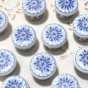 May include: A collection of white and blue ceramic cabinet knobs. Each knob features a detailed blue floral design on a white background. The knobs have a round shape and are mounted on silver-toned hardware. Ideal for adding a decorative touch to furniture.