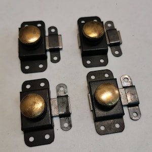 Può includere: Quattro fermagli per porte di armadio in metallo nero con pomelli dorati. Ogni fermaglio ha una base rettangolare con quattro fori e un fermo a cerniera.