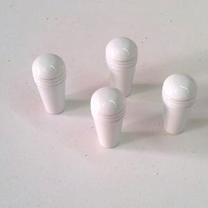 Op de afbeelding: Vier witte keramische knoppen met een afgeronde bovenkant en een gegroefd ontwerp. De knoppen zijn in een vierkant patroon op een wit oppervlak gerangschikt.
