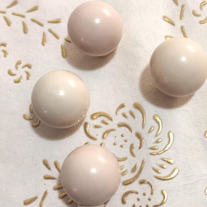 May include: Four round, pale pink, ceramic knobs with a glossy finish. The knobs are arranged on a white fabric background with a gold floral pattern.