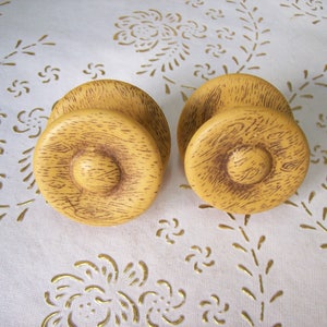 Peut inclure: Deux boutons ronds en bois pour armoire avec une finition texturée en grain de bois. Les boutons sont de couleur brun clair avec un centre brun foncé.