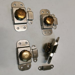 May include: Four silver-toned metal catches with brass knobs. Each catch has a small metal loop on the side. One catch is separated from the others and is lying on its side. A small silver-toned metal piece is also included.