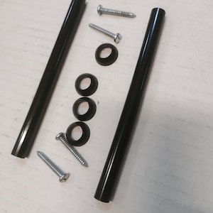 May include: An assortment of hardware components, including two black cylindrical rods, three black washers, and three silver screws, arranged on a light-colored surface. The components appear to be new and unused.