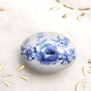 May include: White ceramic knob with a blue floral design. The knob features a large blue flower with smaller blue flowers and leaves surrounding it.