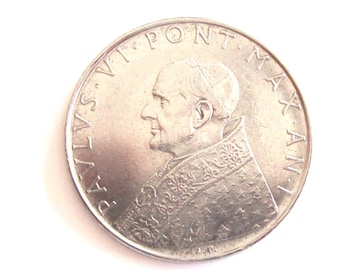 May include: A silver coin with a profile of Pope John Paul II on the obverse. The coin has the inscription "PAX VI PONT. MAX. AN. I" around the edge.