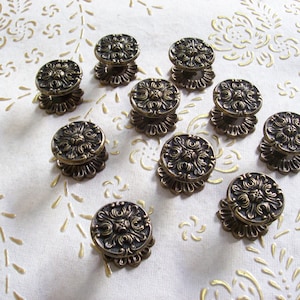 Peut inclure: Dix boutons de tiroir en laiton de style antique avec des motifs floraux ornés. Chaque bouton a une base ronde et un motif floral surélevé et détaillé.